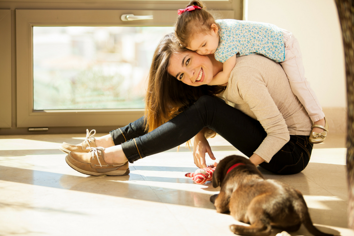 child on teens back who is sitting on floor playing with a puppy