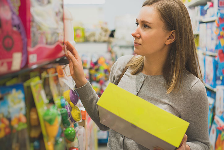 Women perusing toy shelf at store with one toy already in hand.