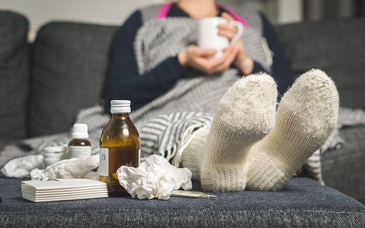 Woman sitting on a couch with her feet propped up on an ottoman. Cold medicine bottles appear next to her feet.