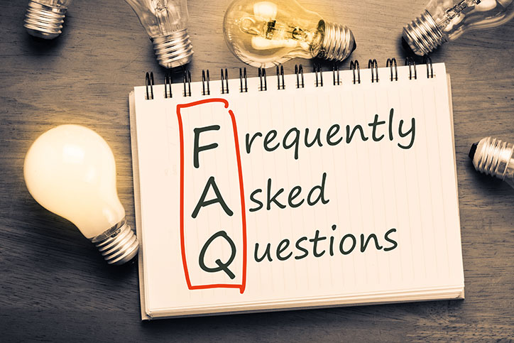 Open spiral-bound notebook on a table surrounded by lightbulbs with the FAQ in Frequently Asked Questions circled in red.