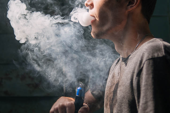 The bottom half of mans face, vaping smoke coming from mouth