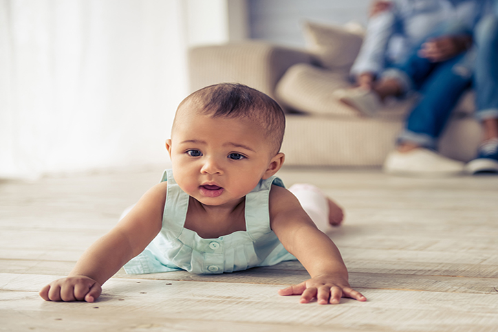 Afro-American baby girl is looking forward with interest while crawling on wooden floor at home