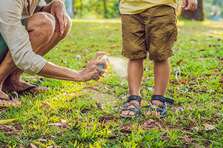 Dad spraying insect repellent on child's leg skin outdoors