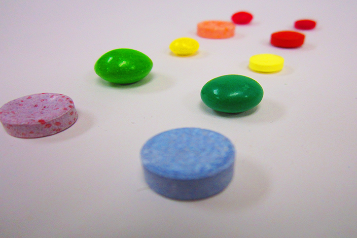 Two rows of colorful circular items, one row is candy and the other row is medicine