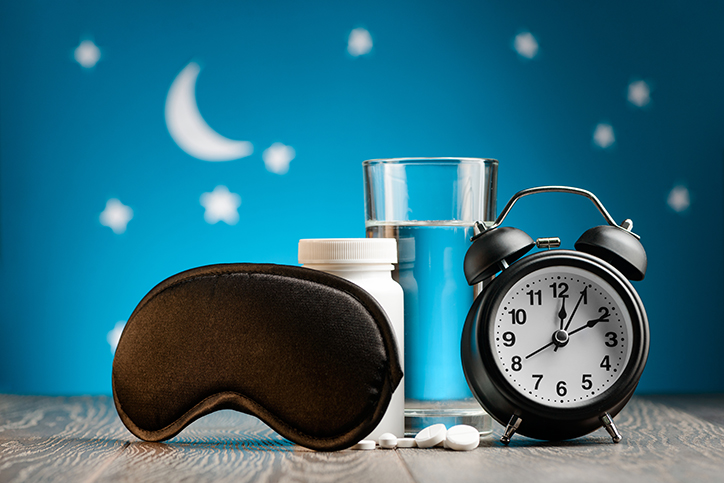 Eye mask, pills and alarm clock on a bedside table over night sky. Getting rid of insomnia, remedies for good restful sleep.