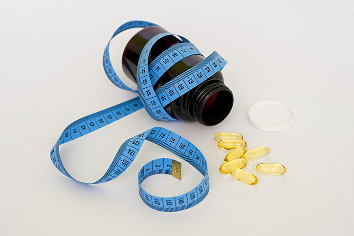 A blue tape measure wrapped around a pill container with some pills laying next to it
