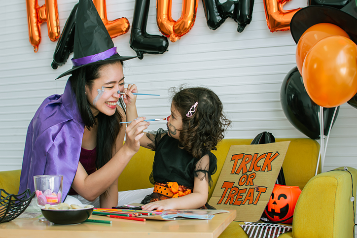 Mother an daughter in Halloween costumes painting each others faces with Halloween decorations in the background