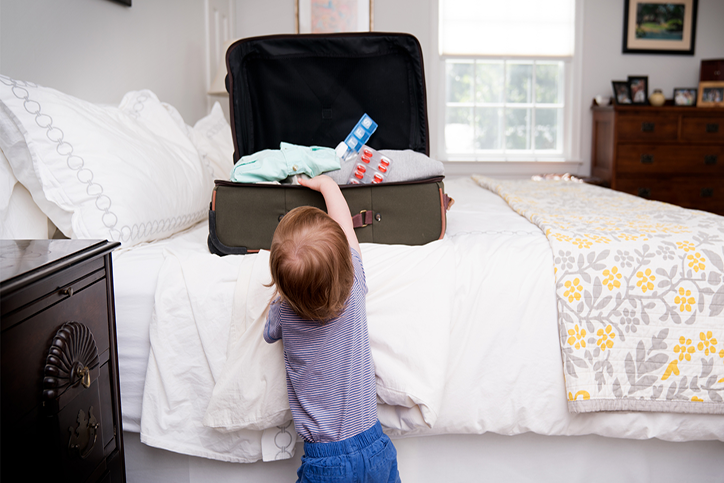 Child reaching into an open suitcase on the bed that contains medicines