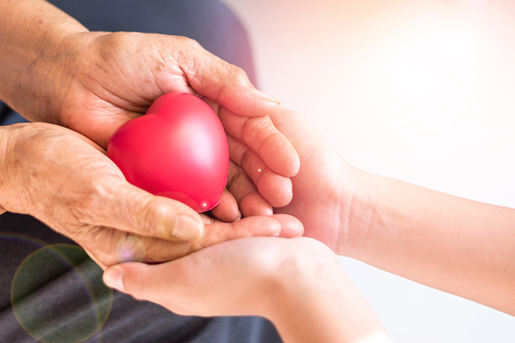 Caregiver hand holding elderly persons hand with a heart