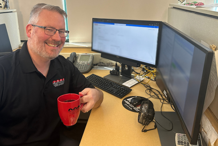 Photo of Robert sitting at a desk with a red coffee cup filled with coffee