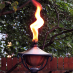 A tiki torch outdoors with a large flame coming out of the top.