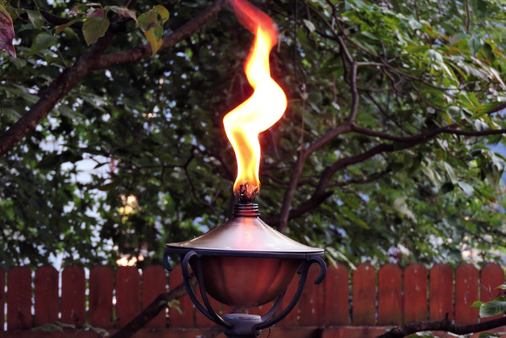 A tiki torch outdoors with a large flame coming out of the top.