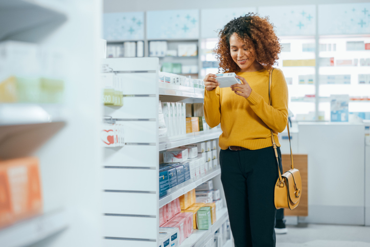 A woman in a drugstore holding a medicine box and reading its label.